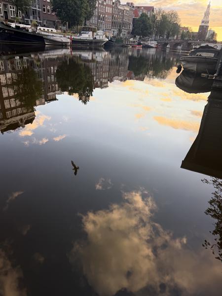 This photo captures a serene morning scene at Oudeschans, Uilenburg, Amsterdam, with historic canal houses and houseboats reflected perfectly in the calm water